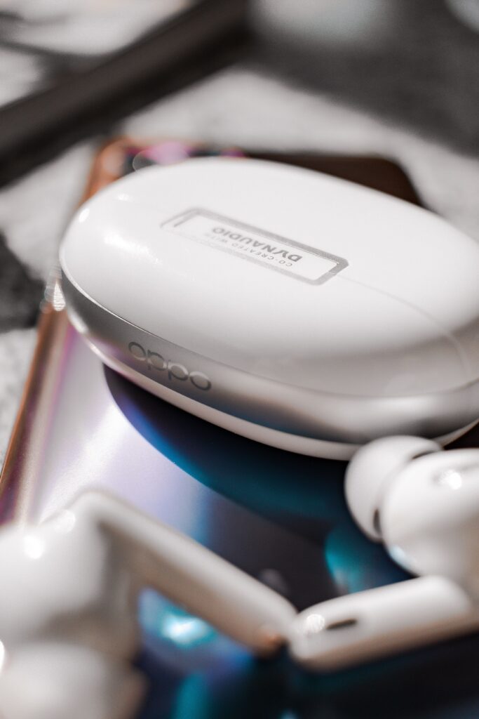 White wireless earbuds and case on a reflective surface with a blurred background.